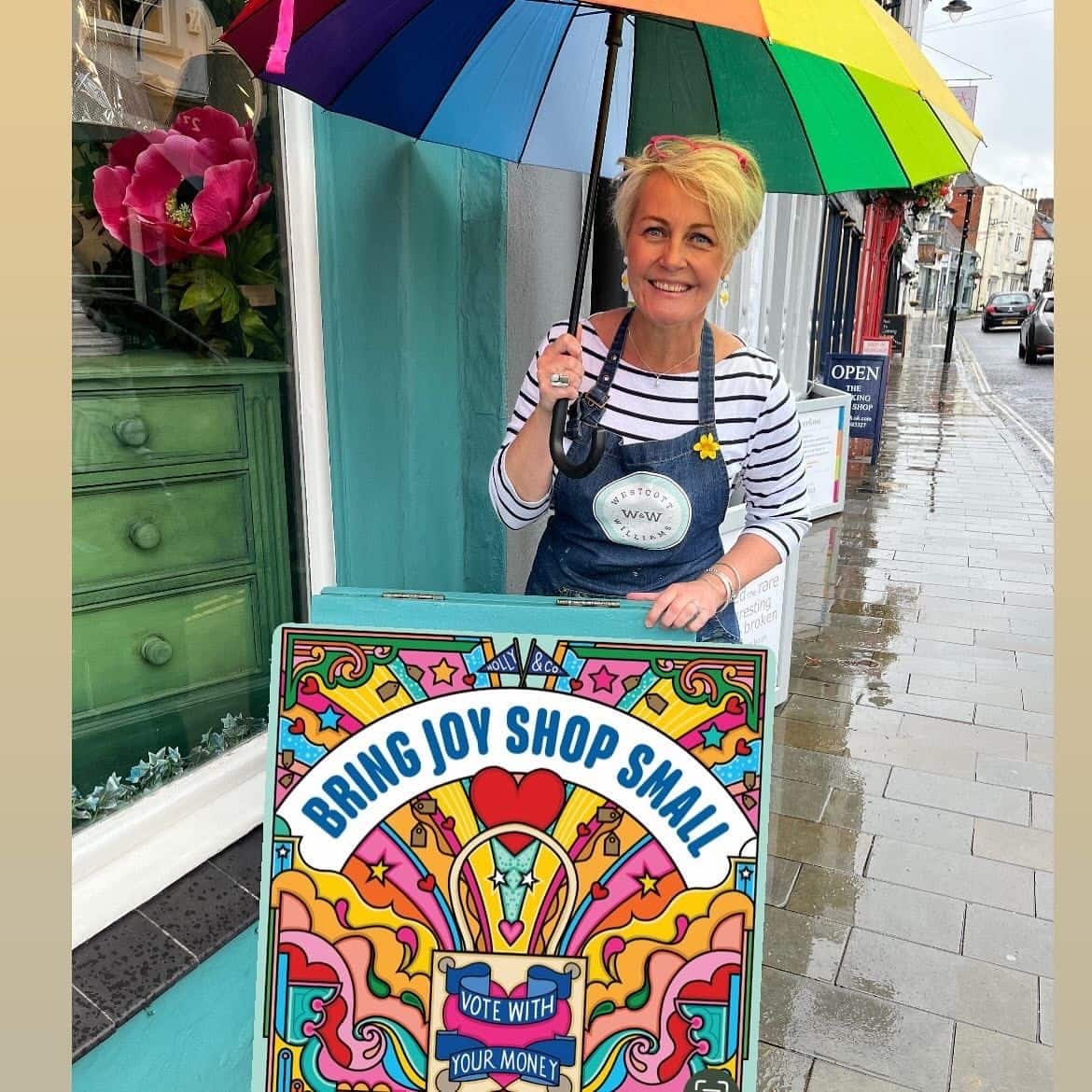 Independent shop owner in Dorking holding rainbow umbrella and Small Business Saturday sign