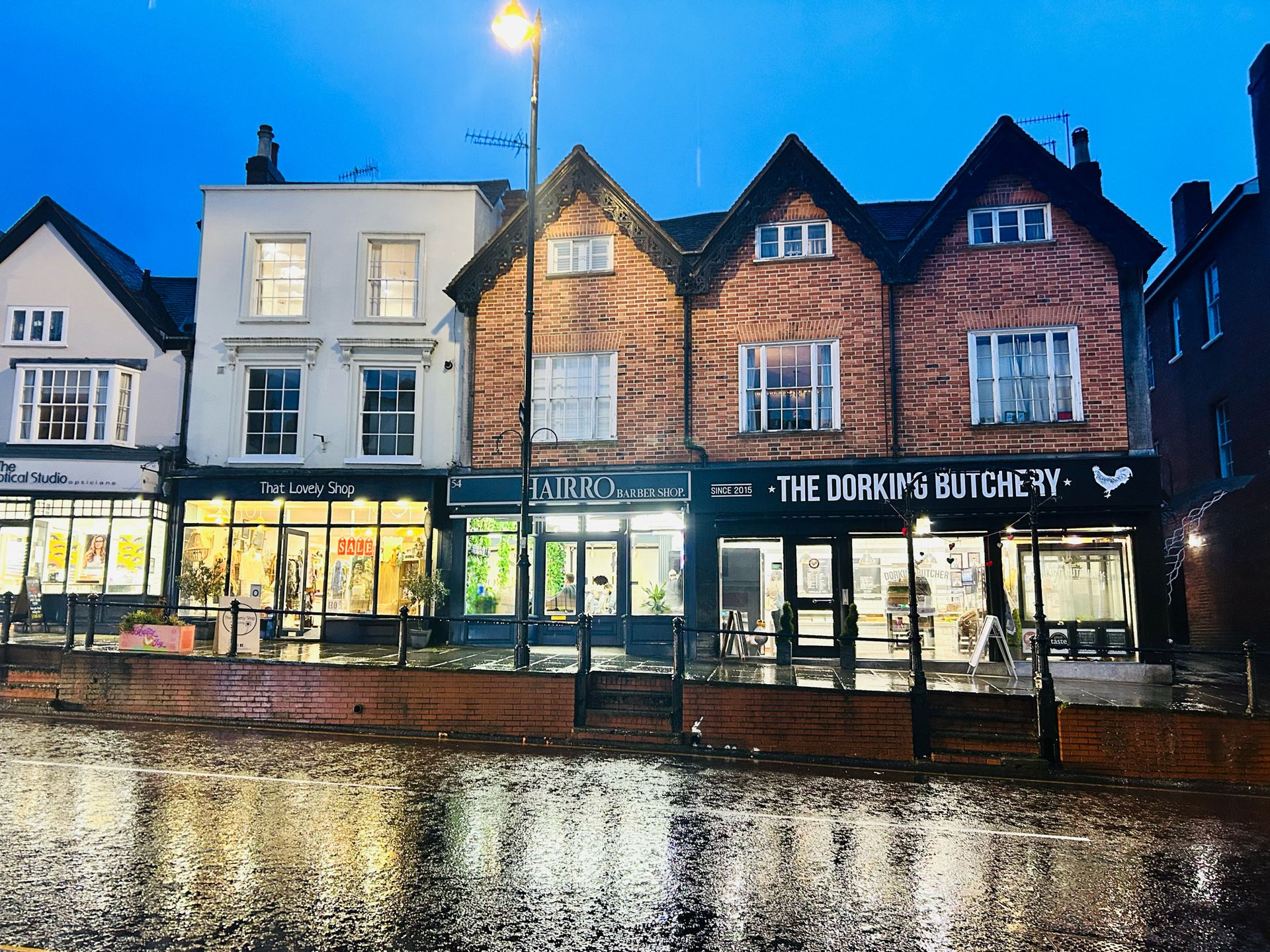 Dorking High Street shops illuminated at dusk with wet pavement reflections