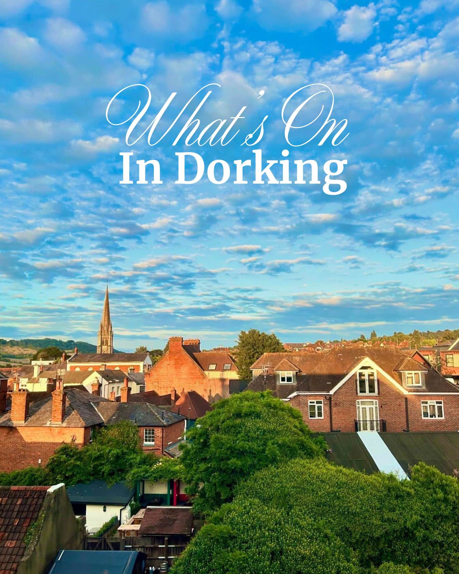 Dorking rooftops with St Martin's Church spire under blue summer sky with white clouds