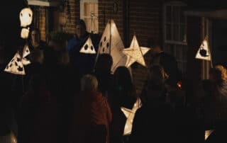 Community members holding illuminated star and pyramid lanterns during evening procession